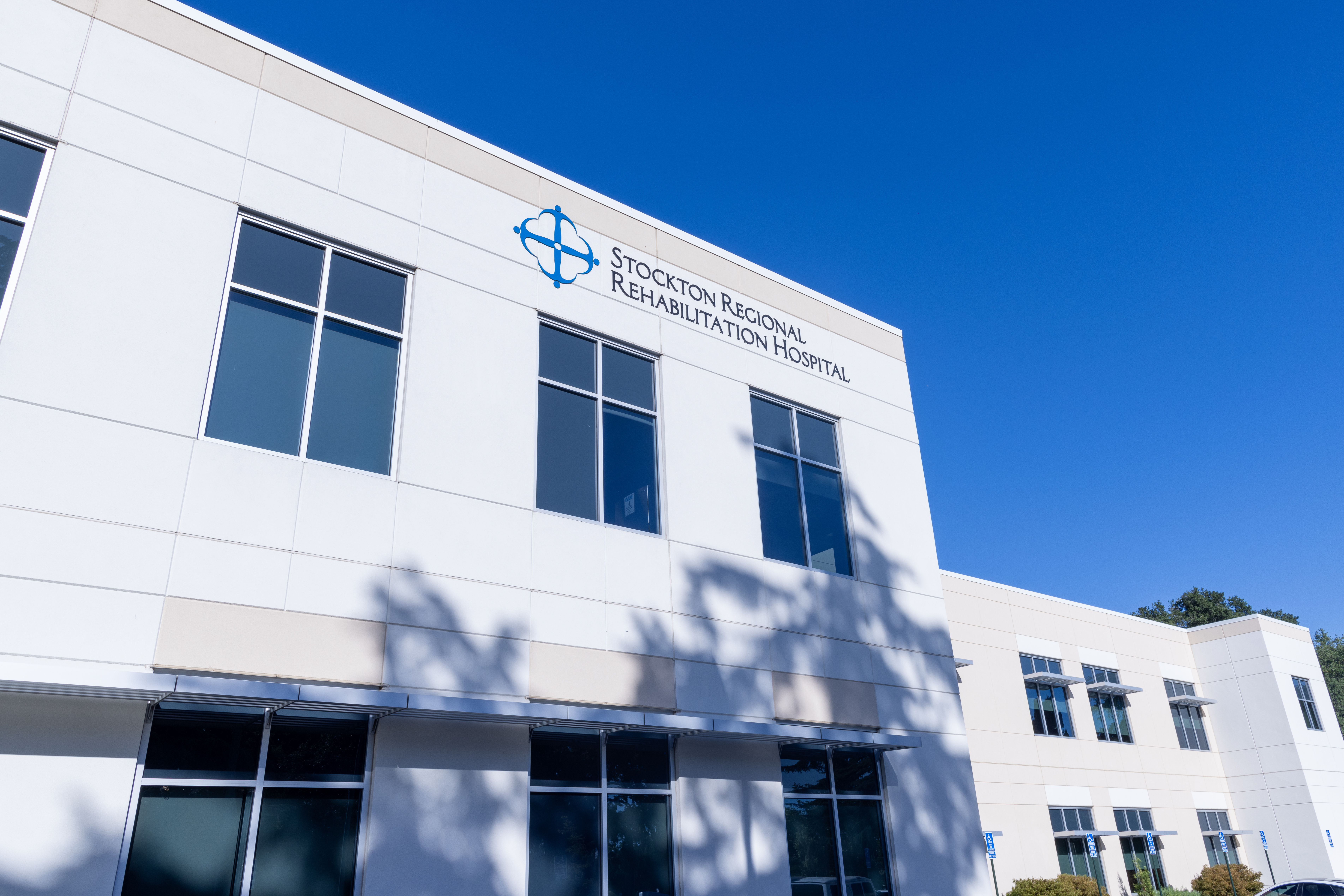  Stockton Regional Rehabilitation Hospital under a clear blue sky. The modern building is marked with the hospital's logo and name prominently displayed, reflecting its role as a key healthcare provider in the region. The hospital's clean and contemporary architecture suggests a welcoming environment for patients and visitors alike.